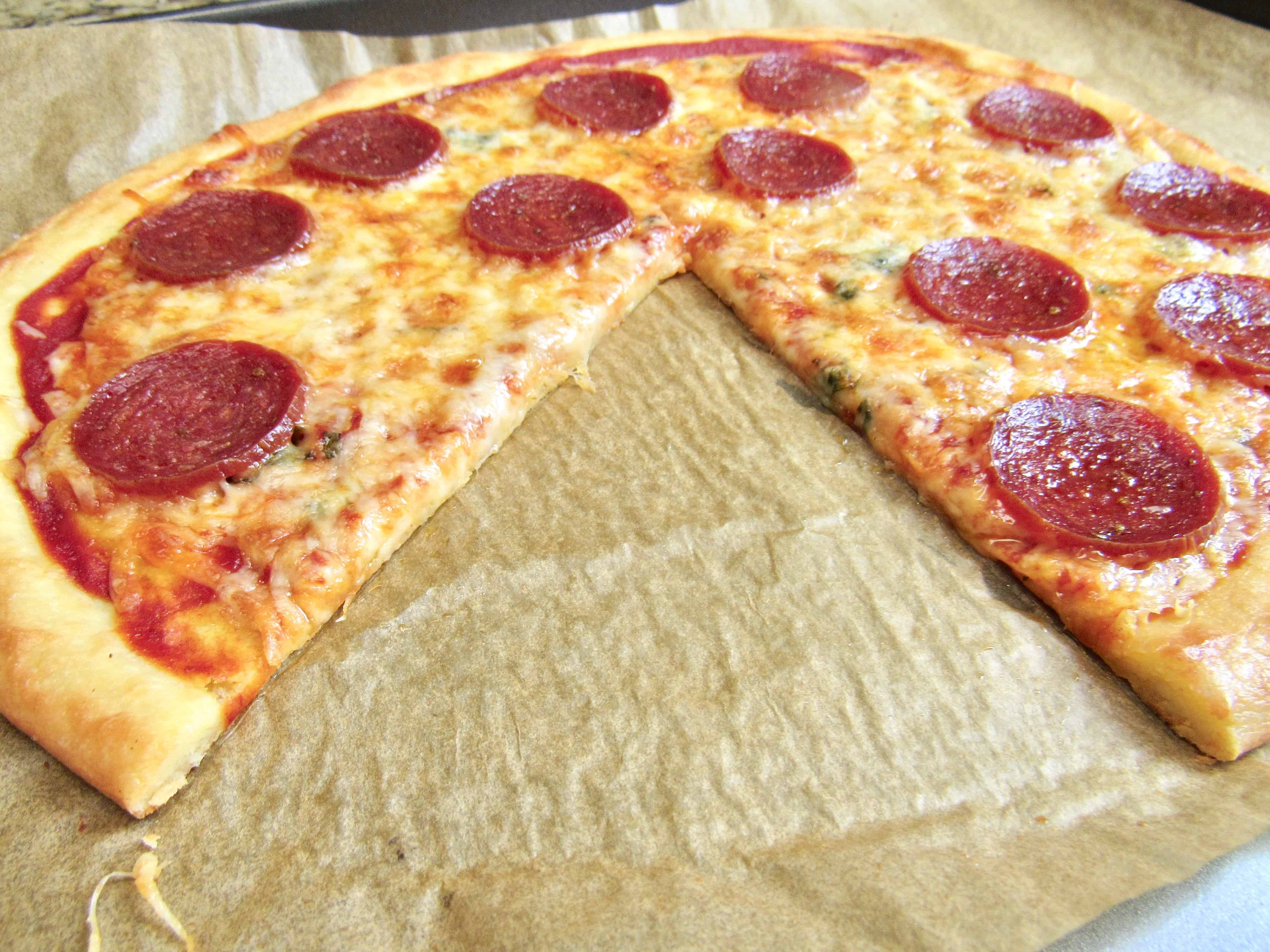 whole fathead pepperoni pizza on sheet pan with parchment with large slice taken out