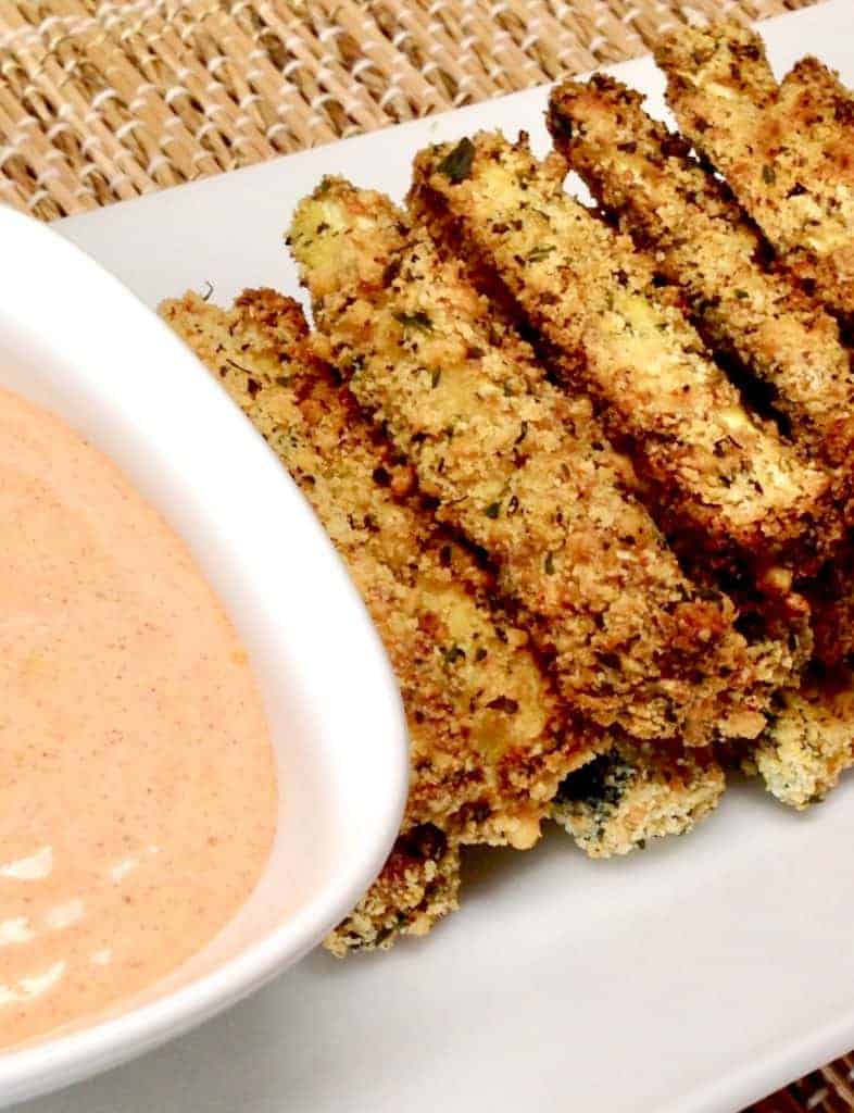 breaded crunchy zucchini sticks on a plate with zipping sauce in a small bowl