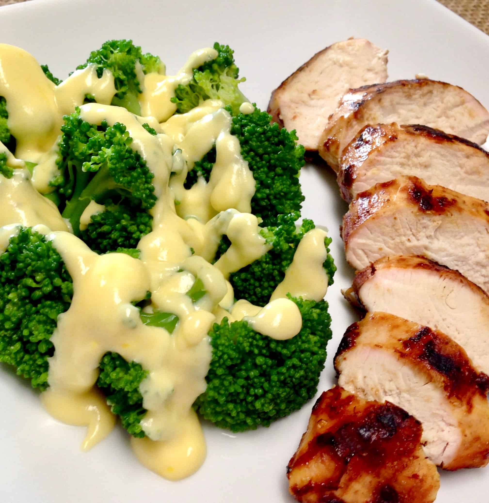 broccoli with cheese sauce next to sliced grilled chicken on white plate