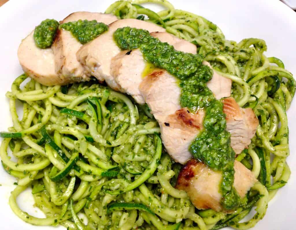zucchini noodles with pesto sauce and sliced grilled chicken over the top