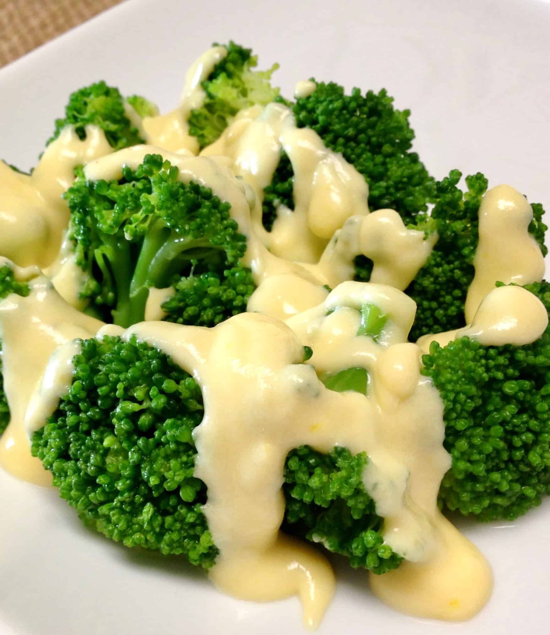 closeup of cheese sauce over broccoli on white plate