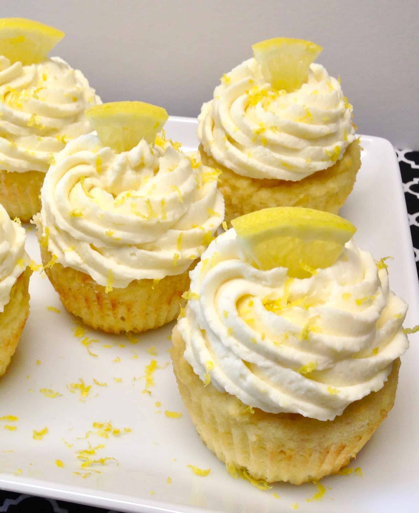 closeup of 4 lemon cupcakes with frosting on white square plate