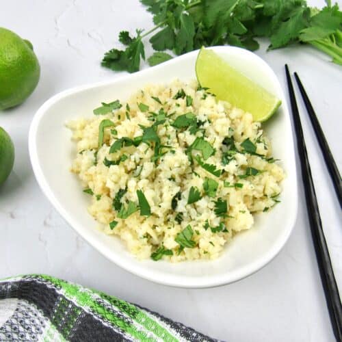 white bowl with lime cilantro cauliflower rice with limes and cilantro garnish