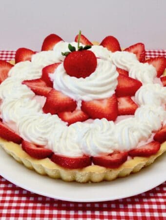 strawberry cream tart decorated with whip cream and fresh strawberries on top