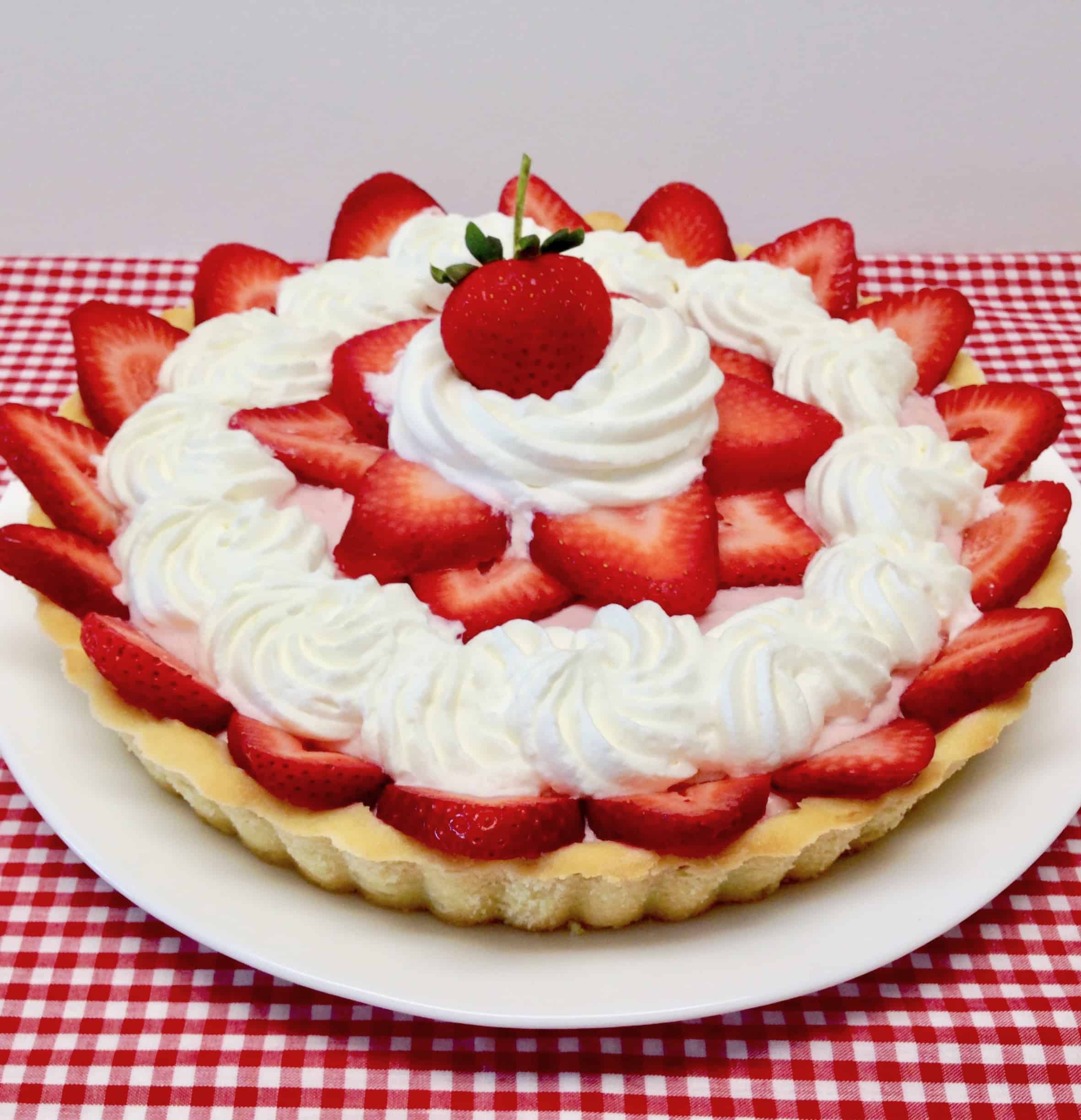 strawberry cream tart decorated with whip cream and fresh strawberries on top