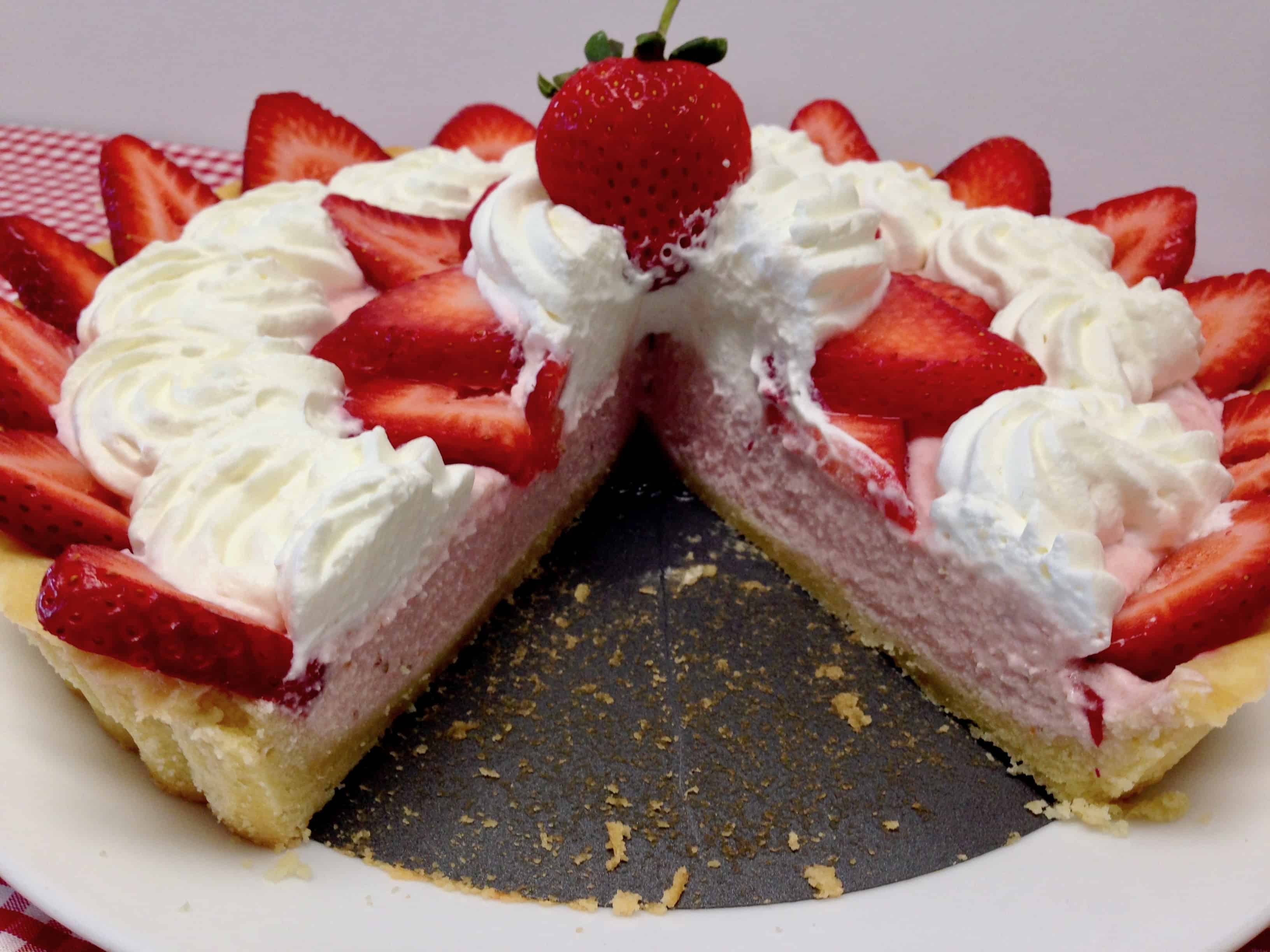 strawberry cream tart with whip cream and strawberries on top and slice missing