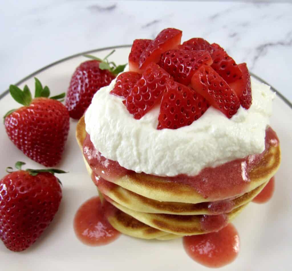 stack of pancakes with strawberry sauce whip cream and strawberries