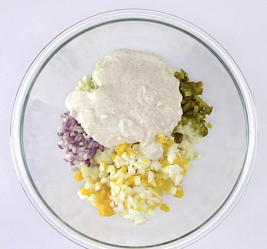 Cauliflower "Potato" Salad ingredients and dressing in glass bowl