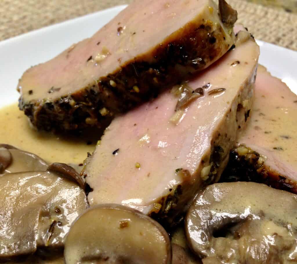 closeup of 3 slices of pork tenderloin on plate with mushrooms