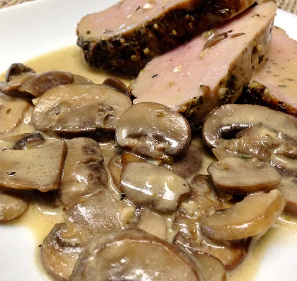 pork tenderloin on white plate with closeup of mushrooms