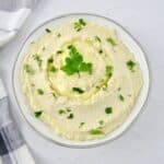 cheesy mashed cauliflower in white bowl with butter and parsley on top