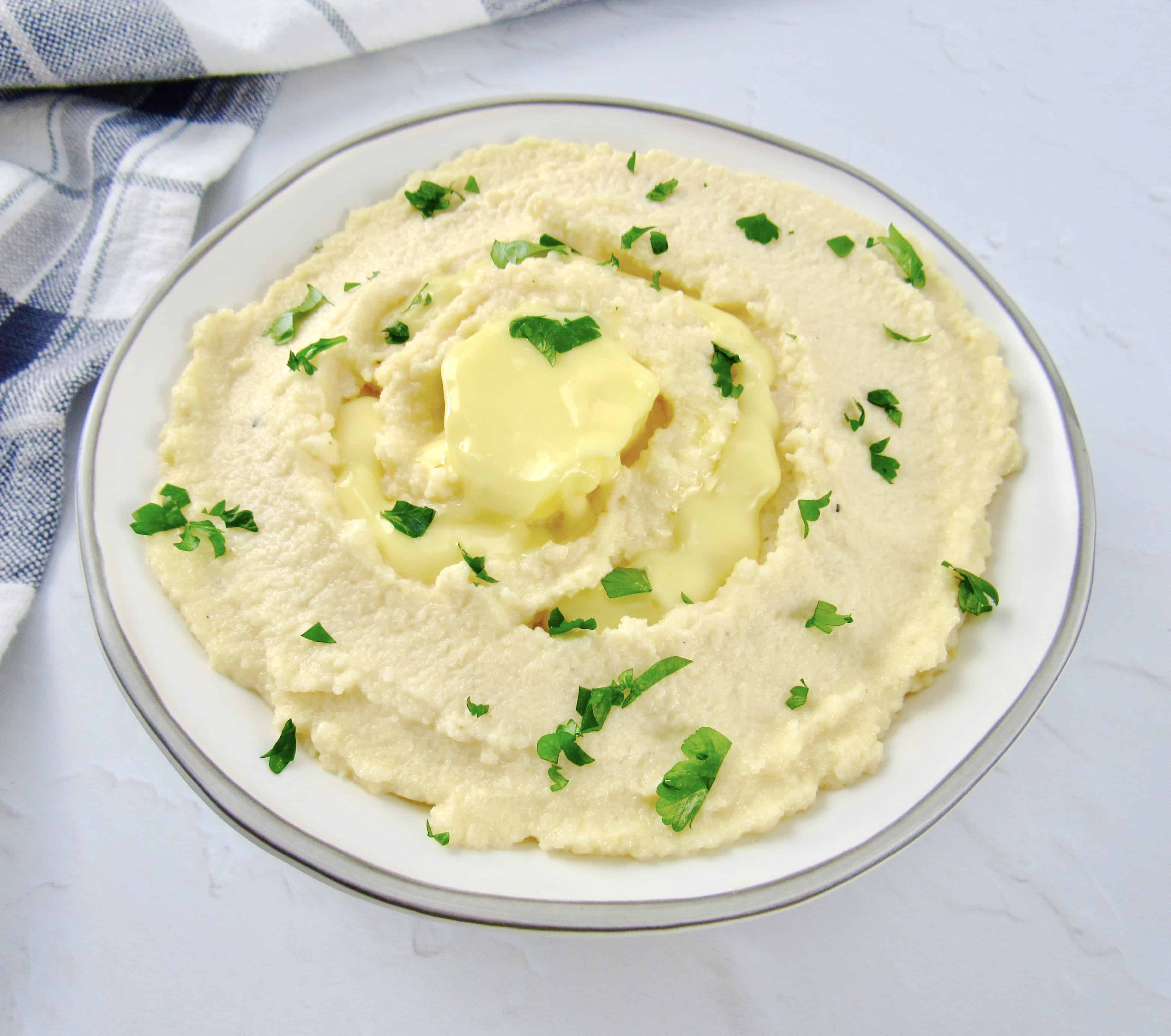 bowl of mashed cauliflower with parsley and butter on top
