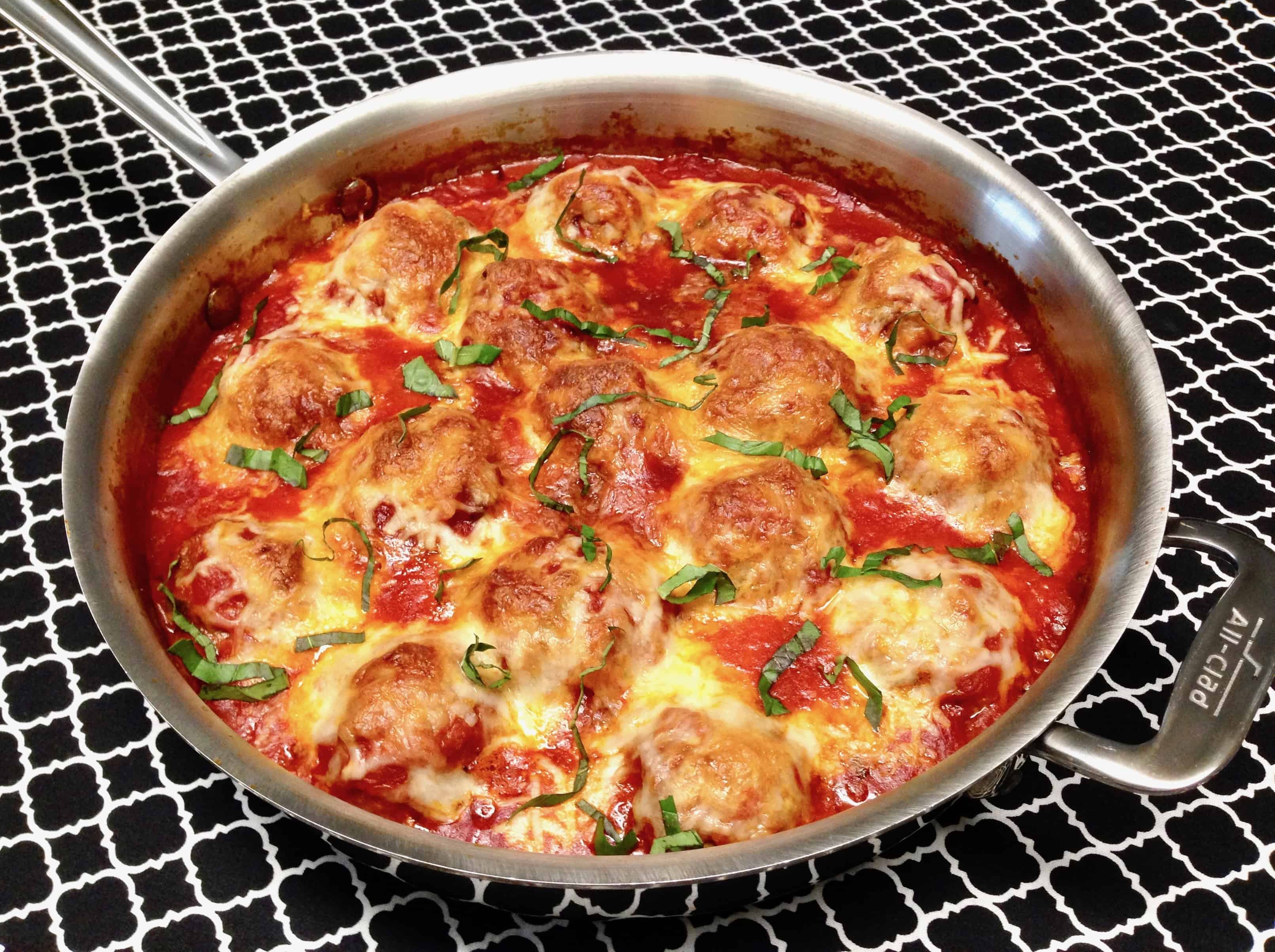 skillet with baked meatballs in sauce with basil garnish