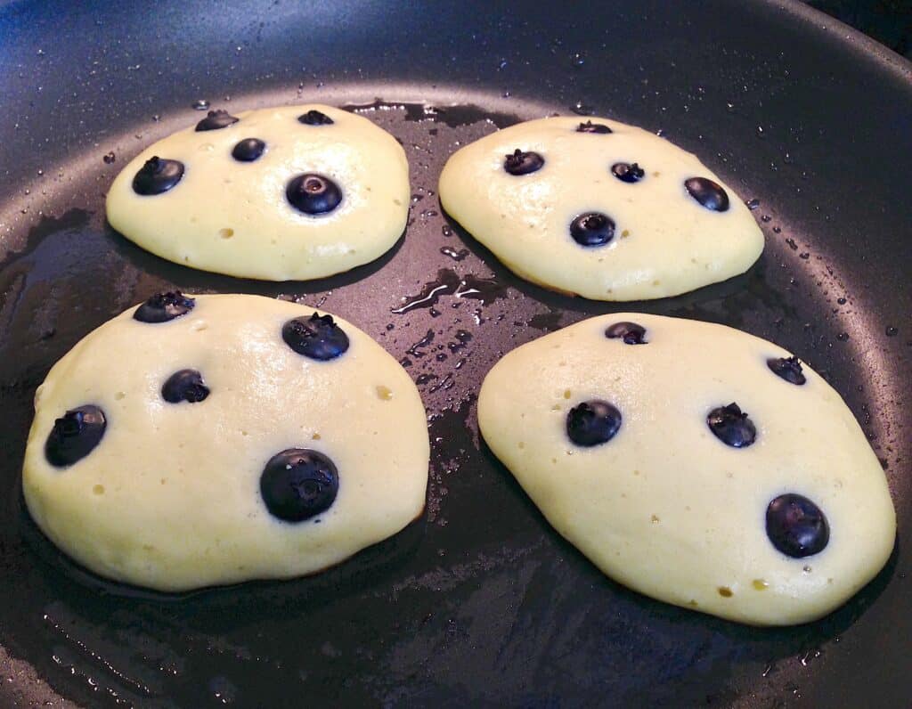 blueberry pancakes being cooked in skillet