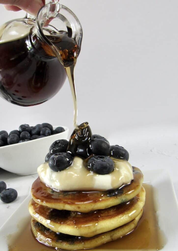 blueberry pancakes on plate with syrup being poured over top