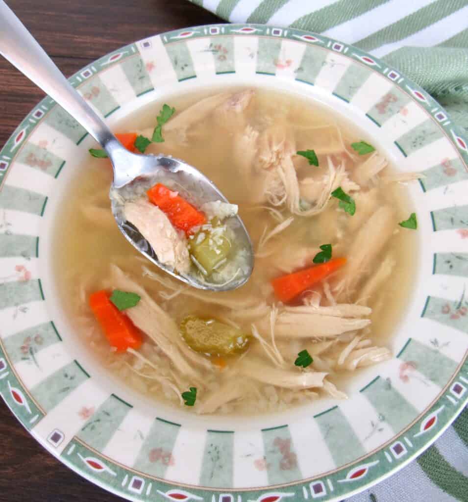 chicken soup with spoon holding up soup over the bowl