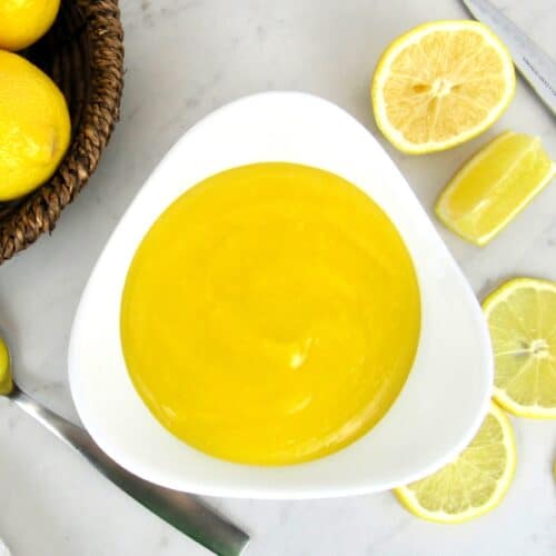 overhead view of lemon curd in white bowl with lemons in the background