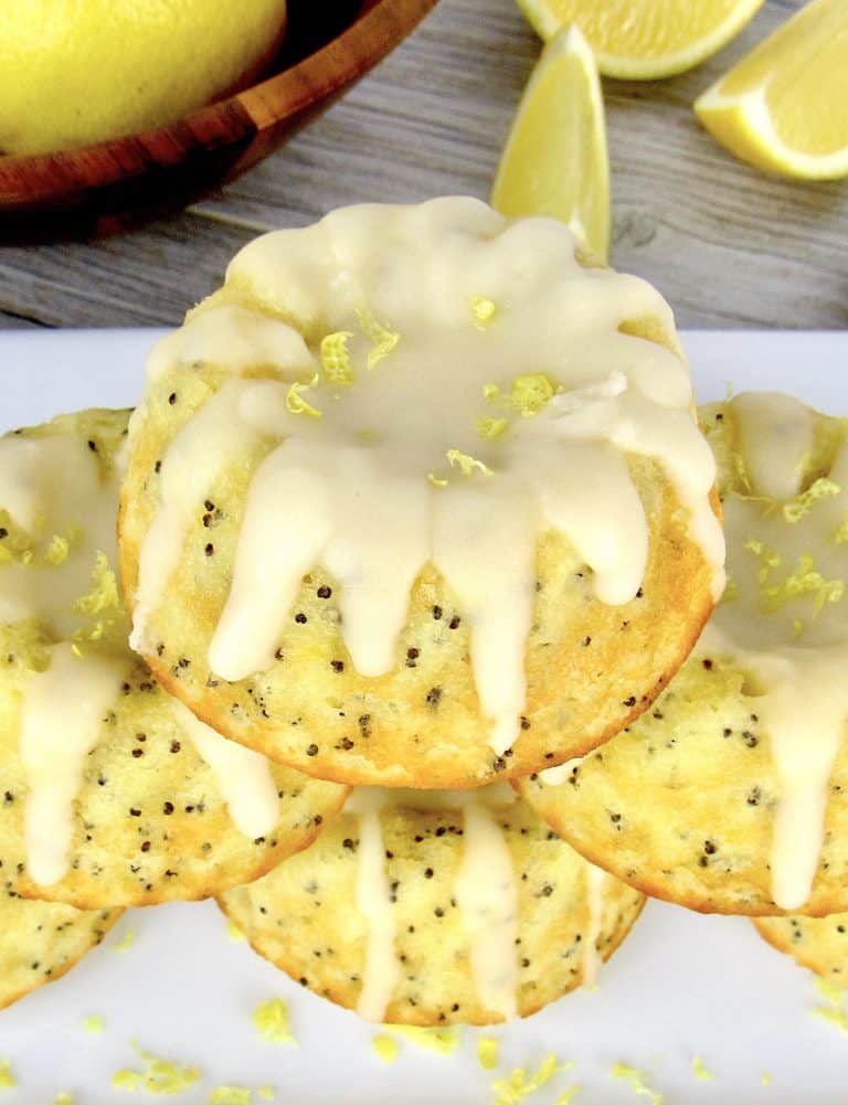 Lemon Poppy Mini Bundt Cakes stacked on white plate with lemon icing dripping off the tops