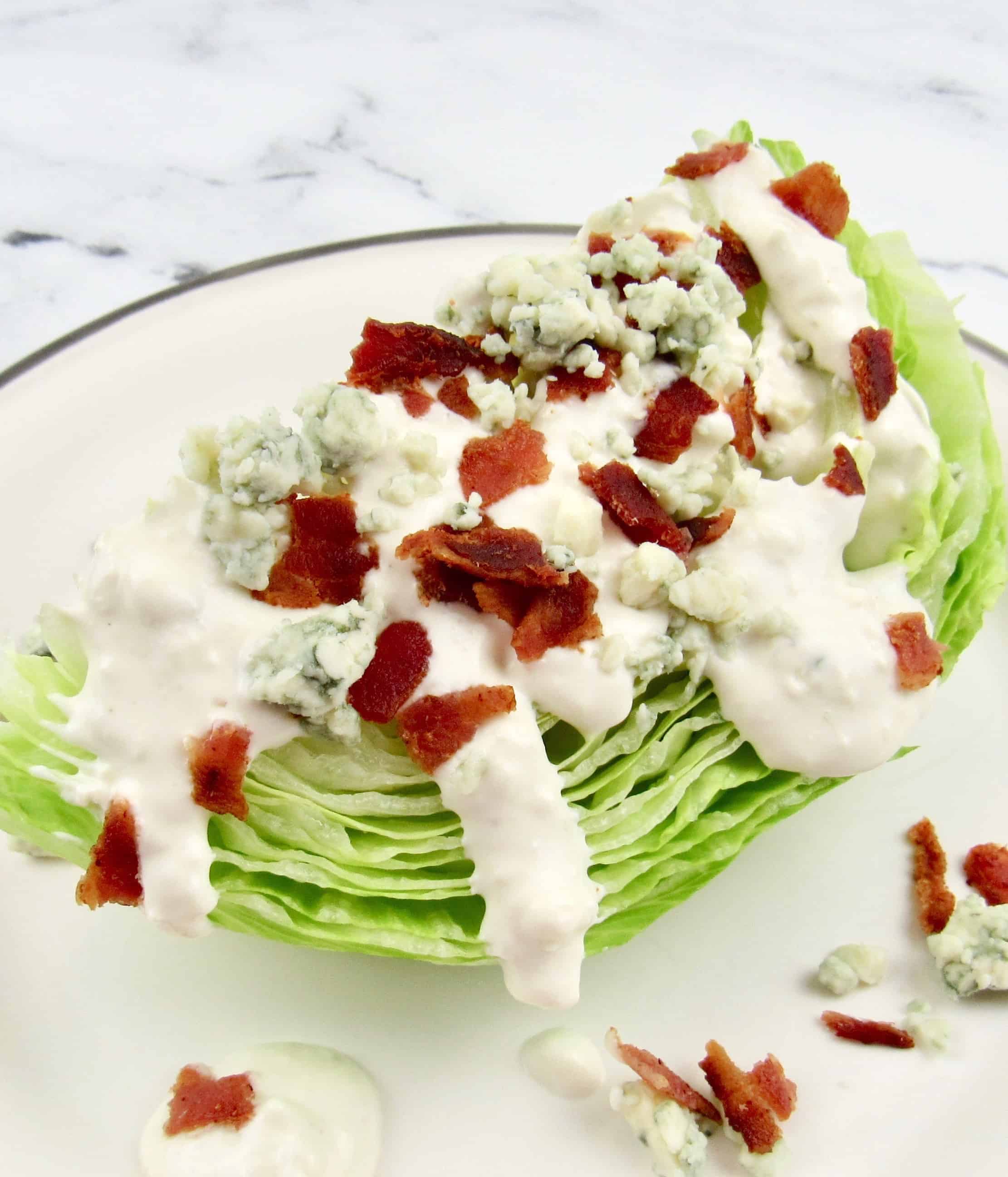 wedge of iceberg lettuce topped with blue cheese dressing, crumbles and bacon