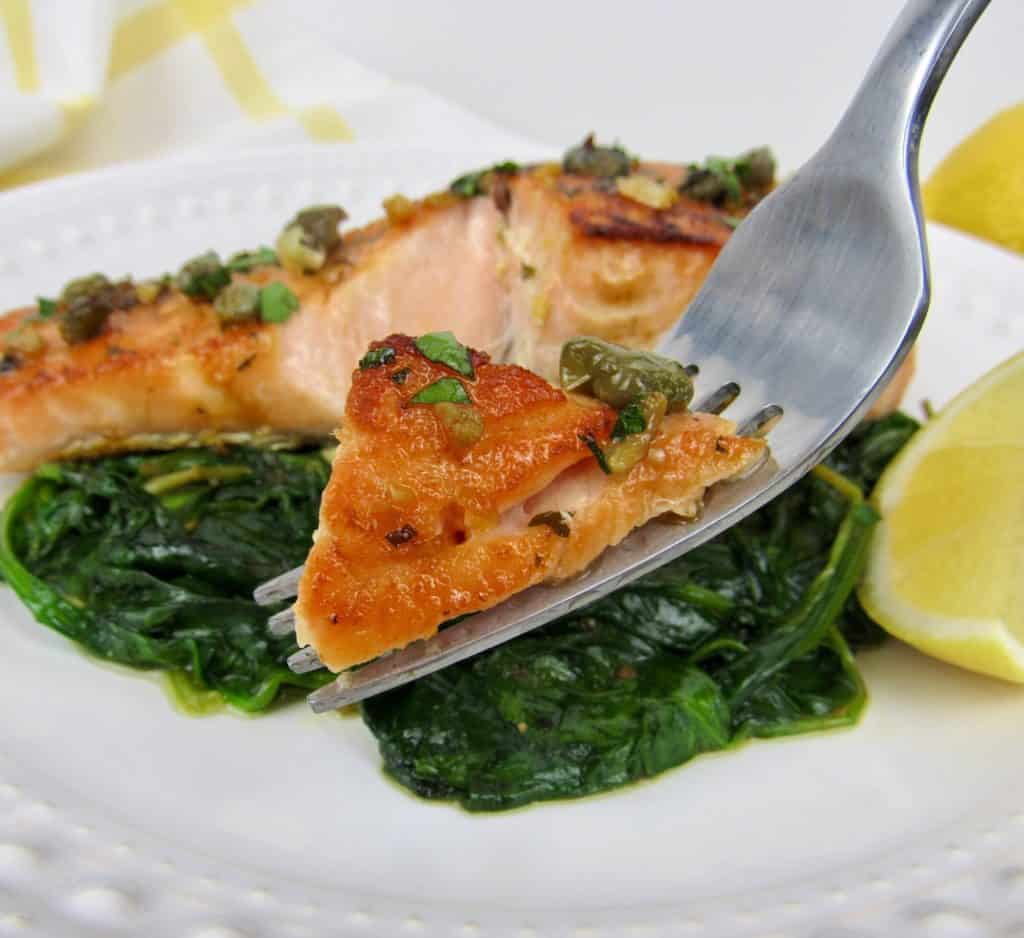 salmon with spinach on white plate with fork holding up some