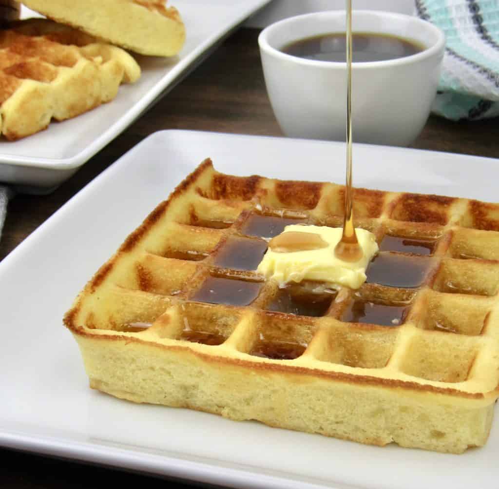 waffle on white plate with butter and syrup being poured on top
