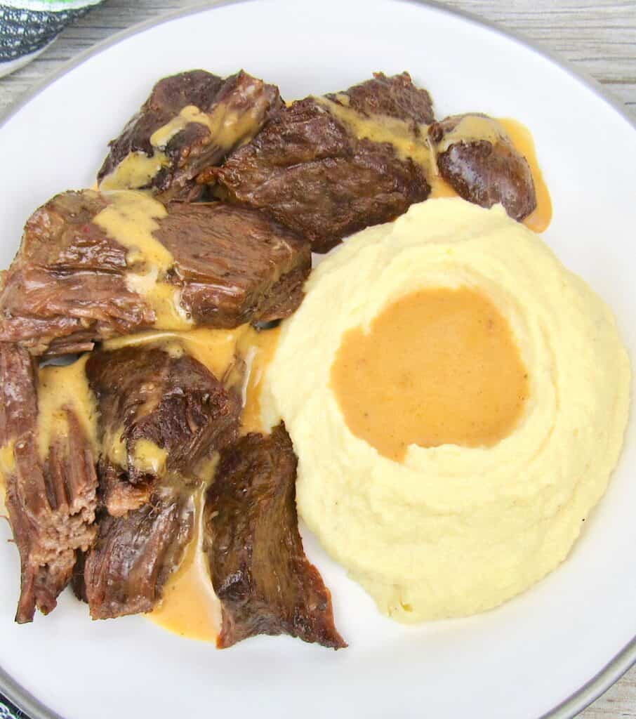 overhead view of pot roast on white plate with gravy and mashed cauliflower