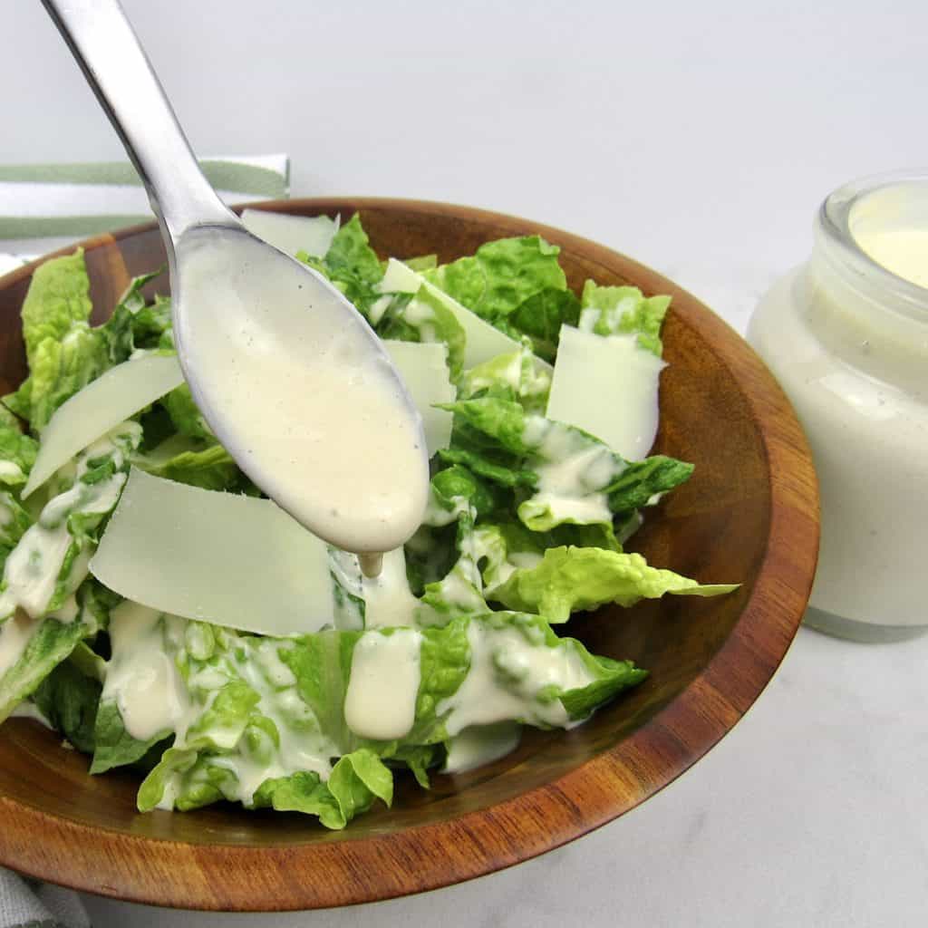 caesar salad with spoon holding up dressing on top