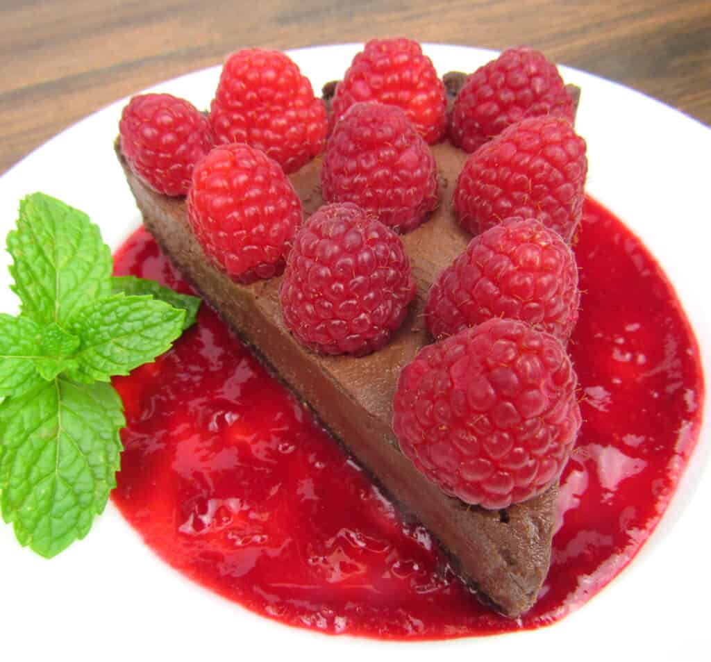 closeup of chocolate tart with raspberries on top sitting in raspberry sauce