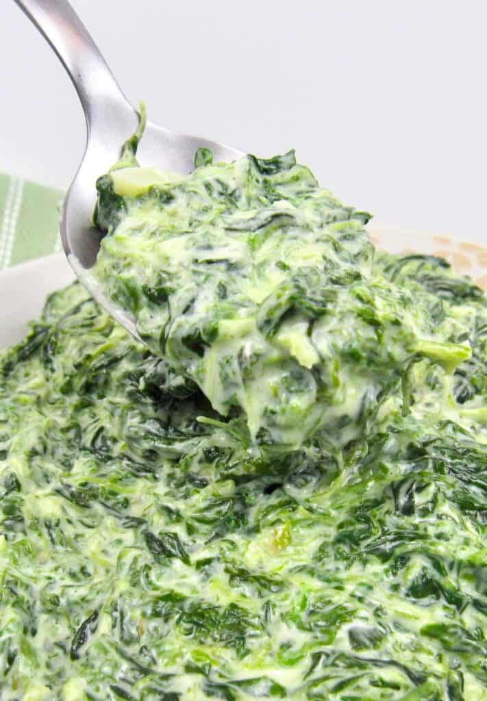 closeup of creamed spinach with spoonful being held up