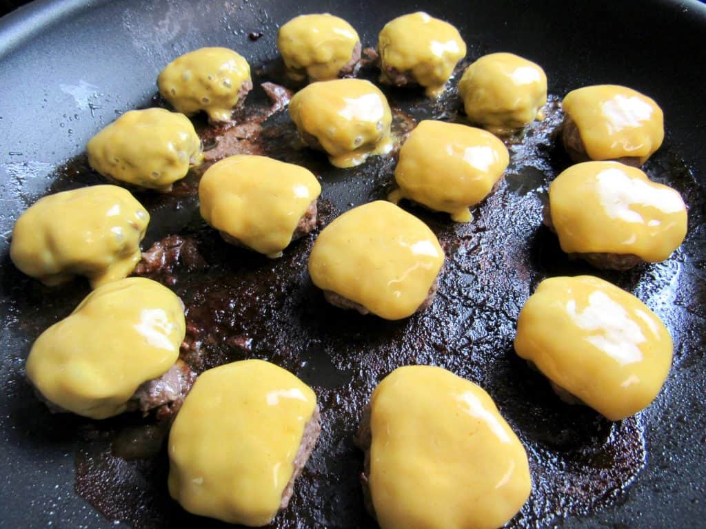 burgers in a pan with melted cheese over the tops