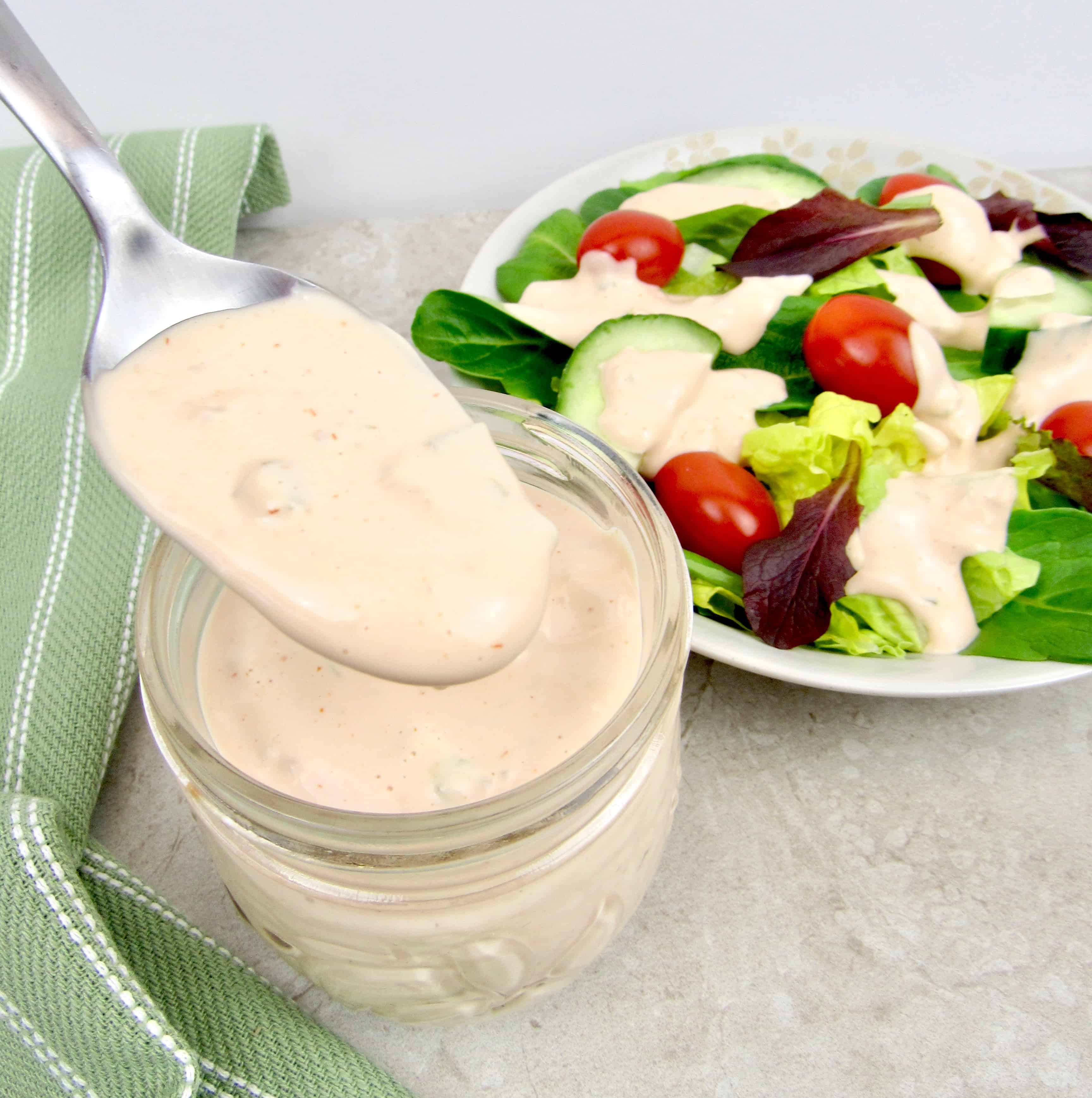 salad with thousand island dressing being pour on with a spoon