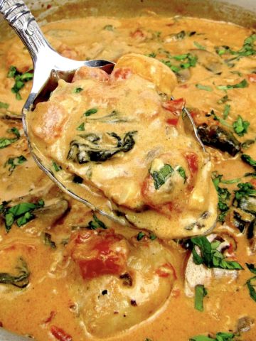 tuscan chicken in skillet with spoon holding up some