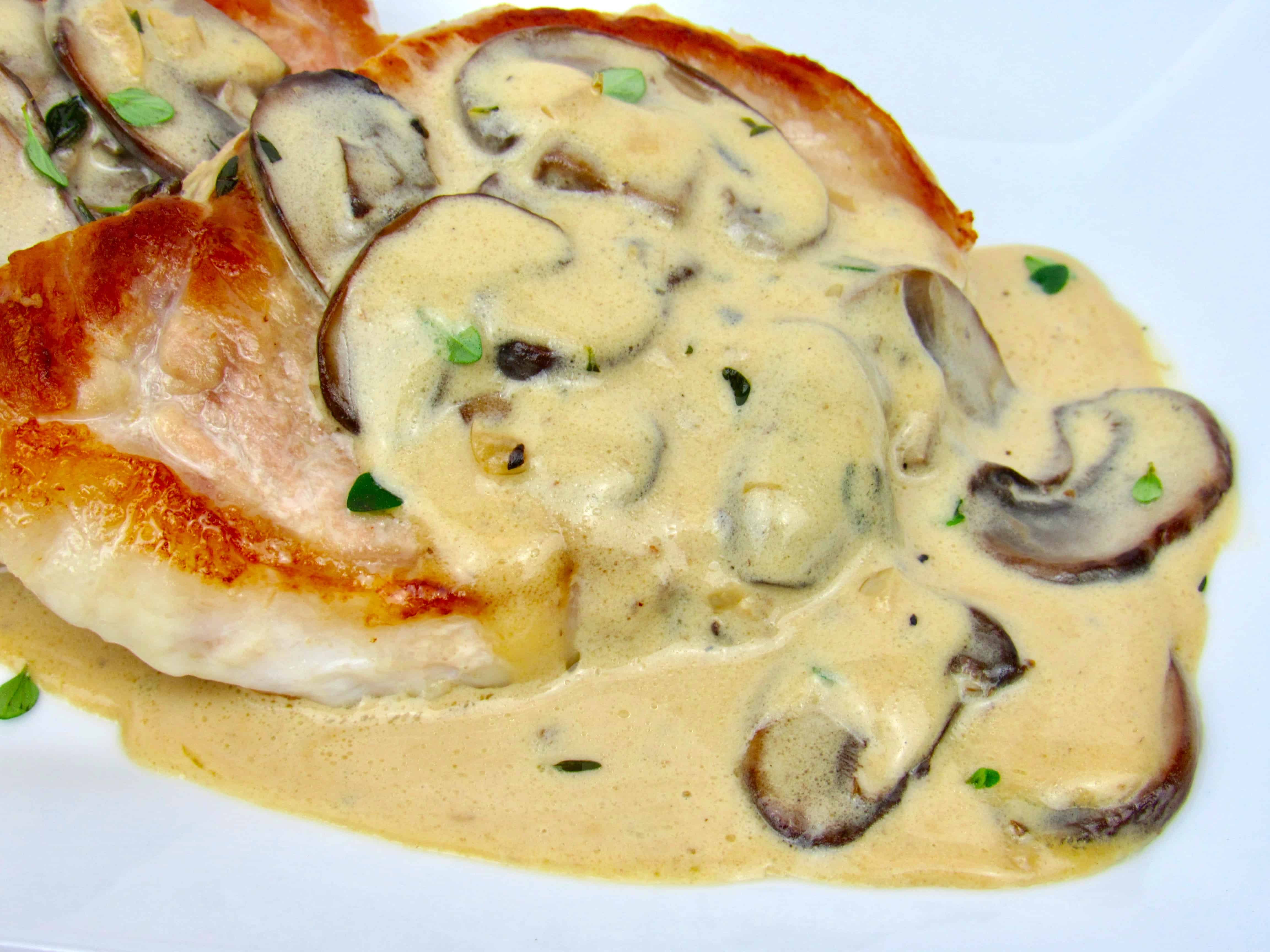 closeup of pork chop with mushroom gravy on top on white plate