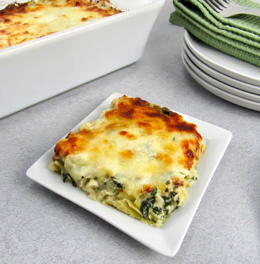 spinach artichoke casserole slice on white plate casserole in background