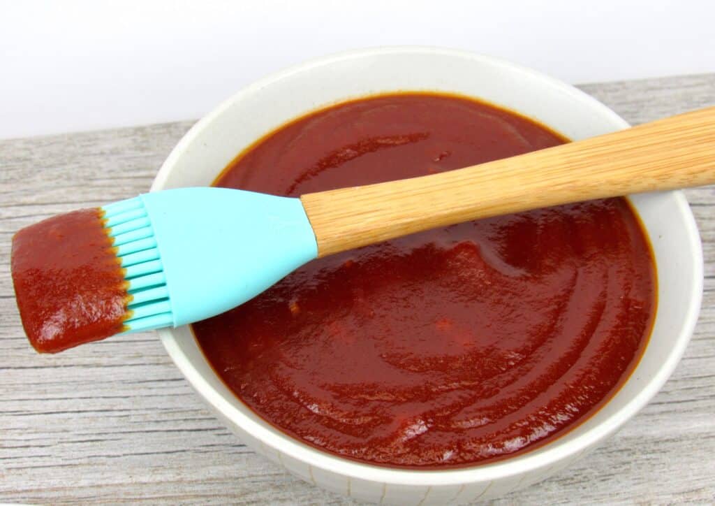 bbq sauce in beige bowl with silicone brush over the side