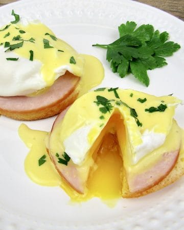 2 Keto Eggs Benedict on white plate with parsley garnish and on egg cut open with runny yolk