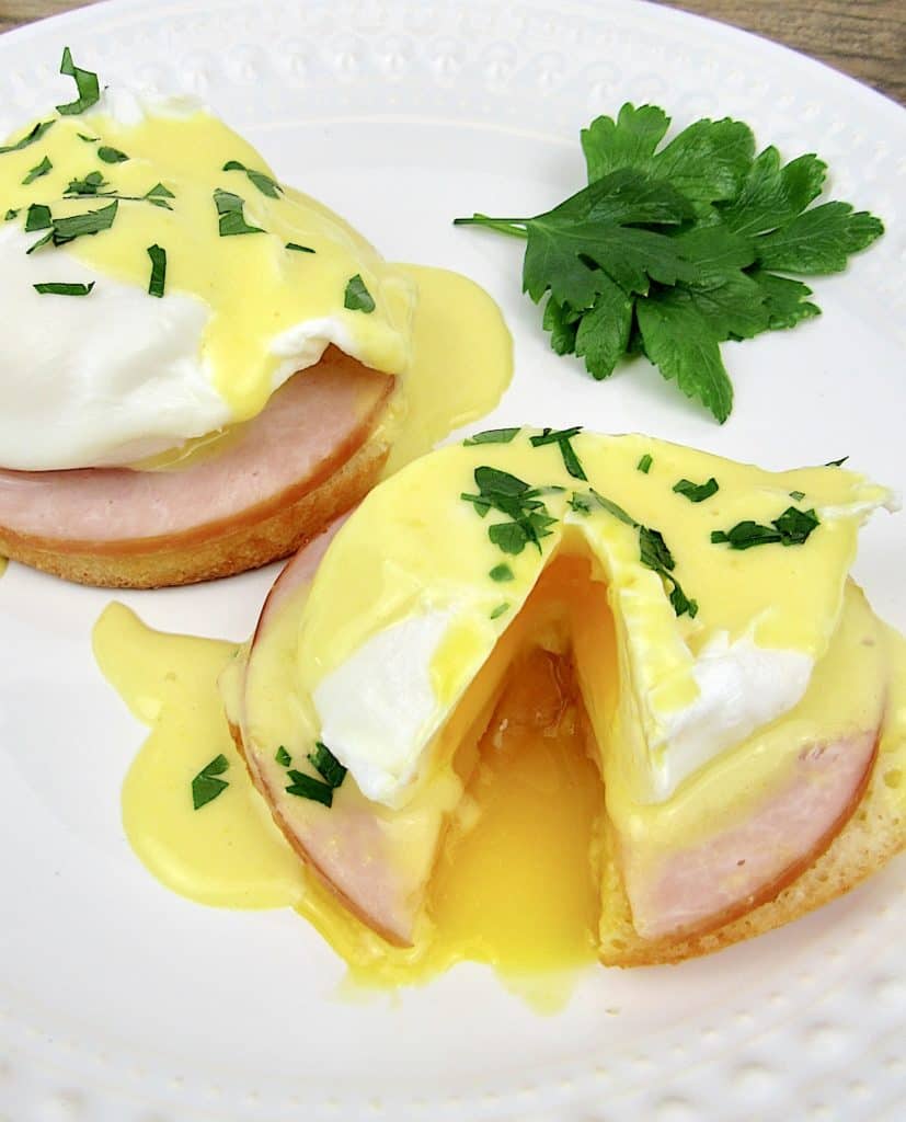2 Keto Eggs Benedict on white plate with parsley garnish and on egg cut open with runny yolk
