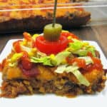 slice of Bacon Cheeseburger casserole on white plate with casserole in background