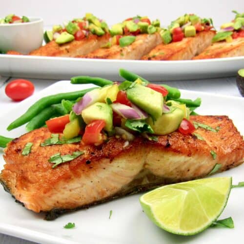 closeup salmon on plate topped with avocado salsa and lime wedge