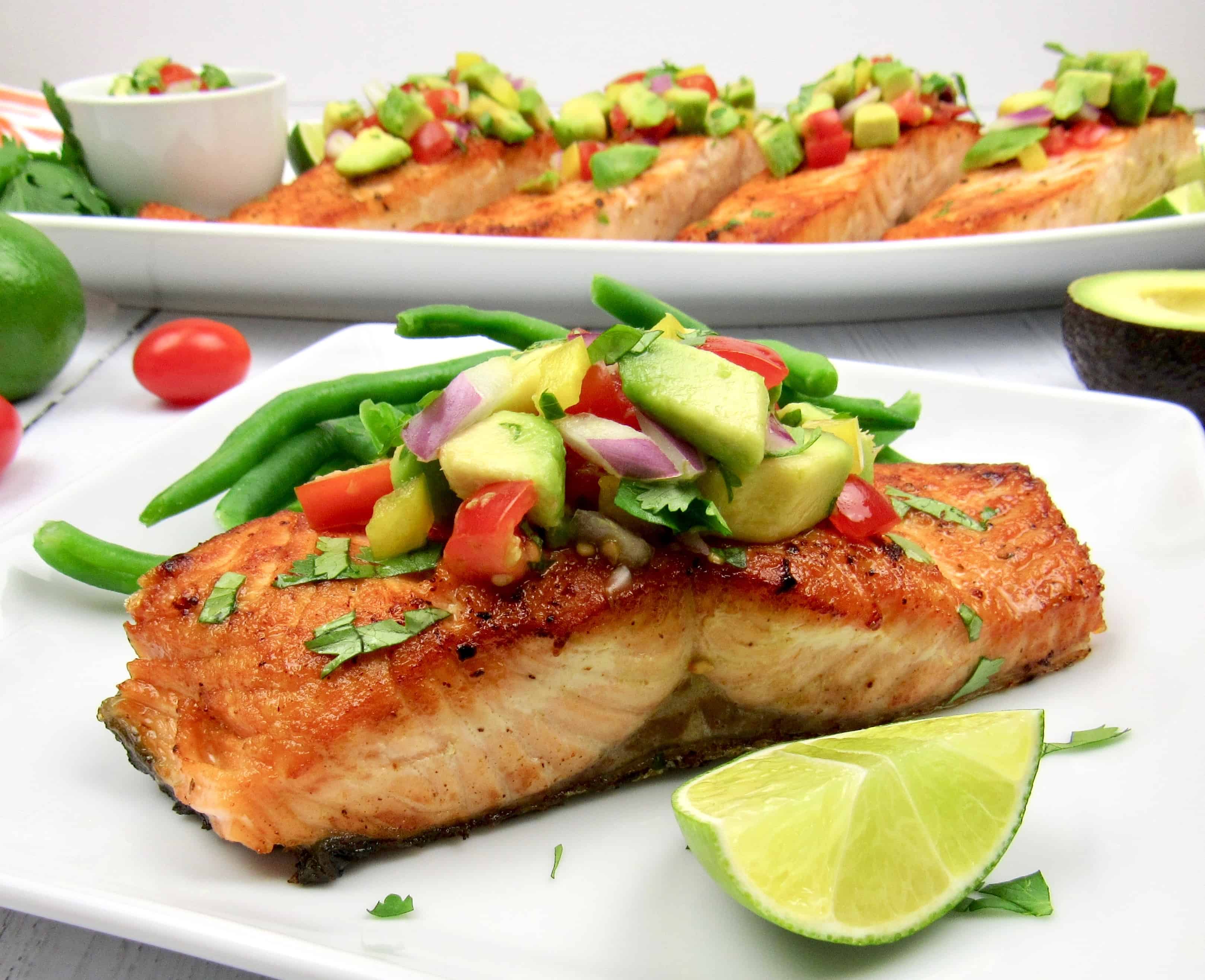 closeup salmon on plate topped with avocado salsa and lime wedge