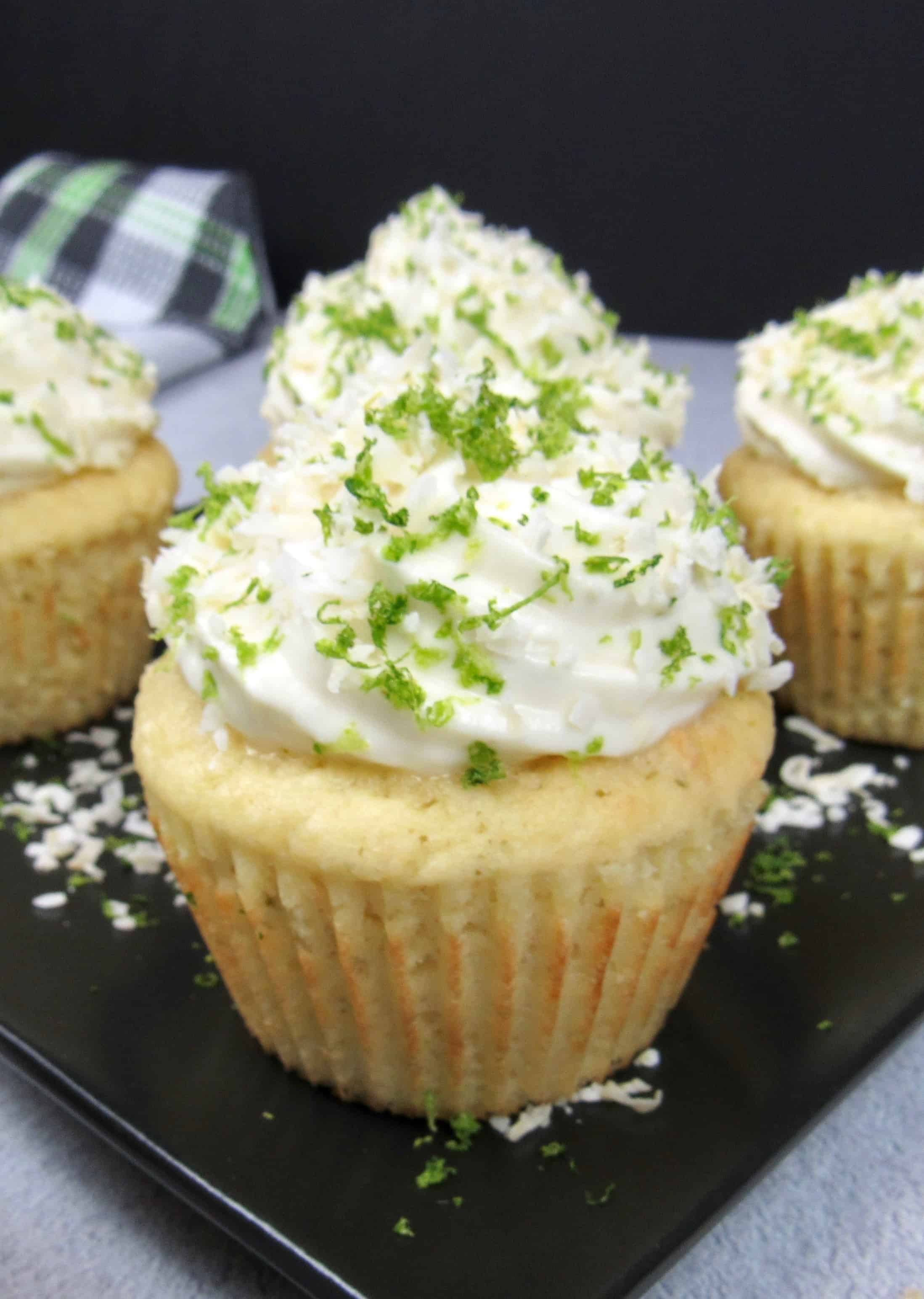 closeup of coconut lime cupcake on a black square plate with frosting, lime zest and coconut flakes on top