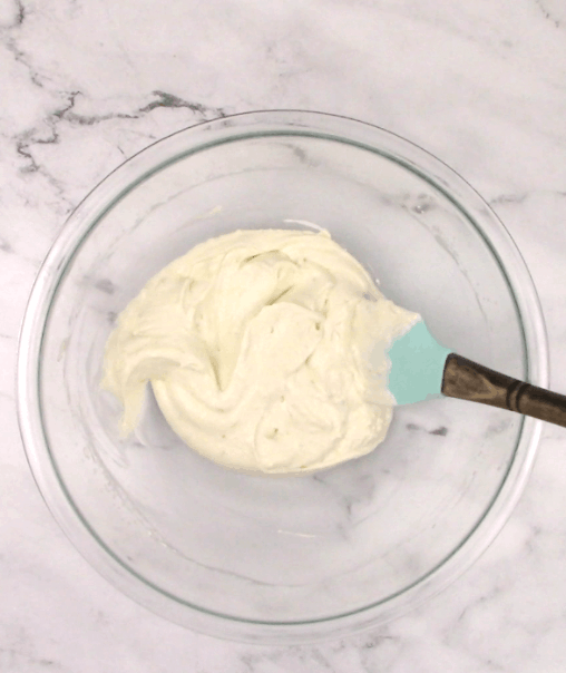 coconut lime frosting in a glass bowl mixed with spatula in the bowl
