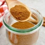 apple pie spice mix being held over glass jar in wooden spoon