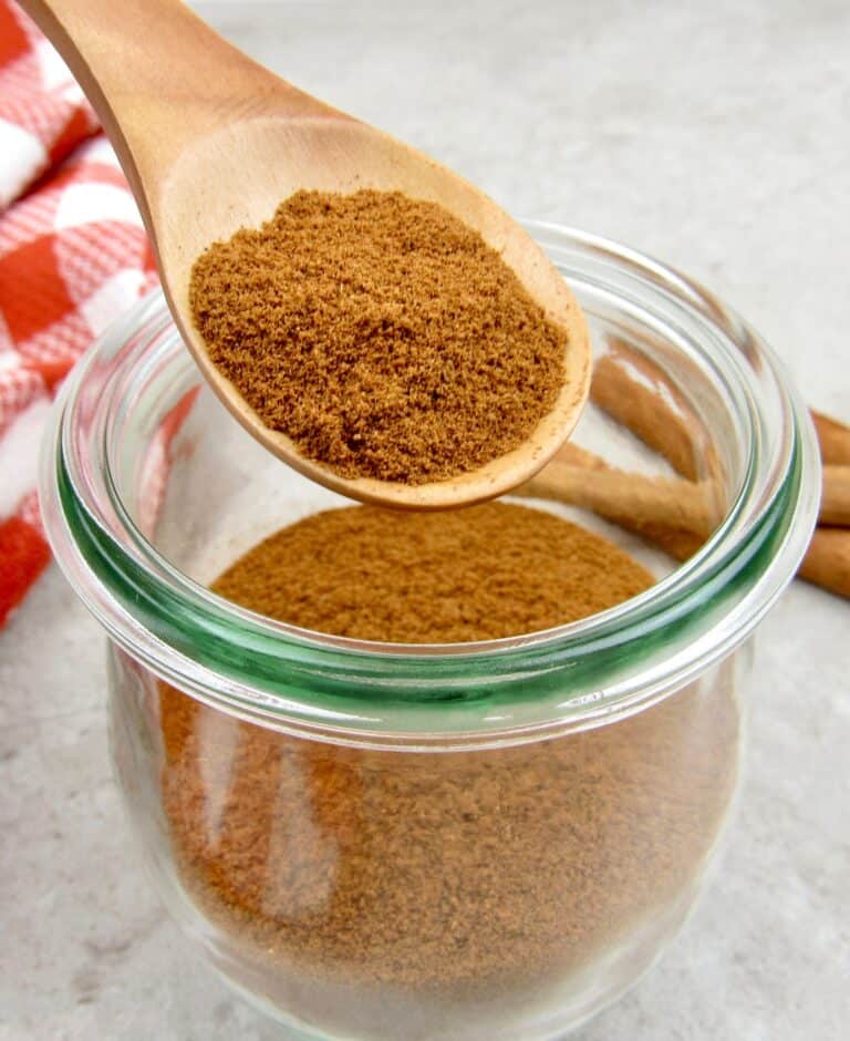 apple pie spice mix being held over glass jar in wooden spoon