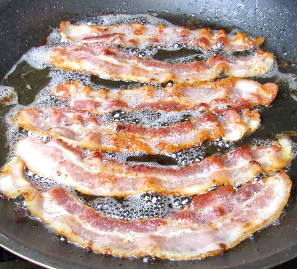 6 pieces of bacon frying in a pan