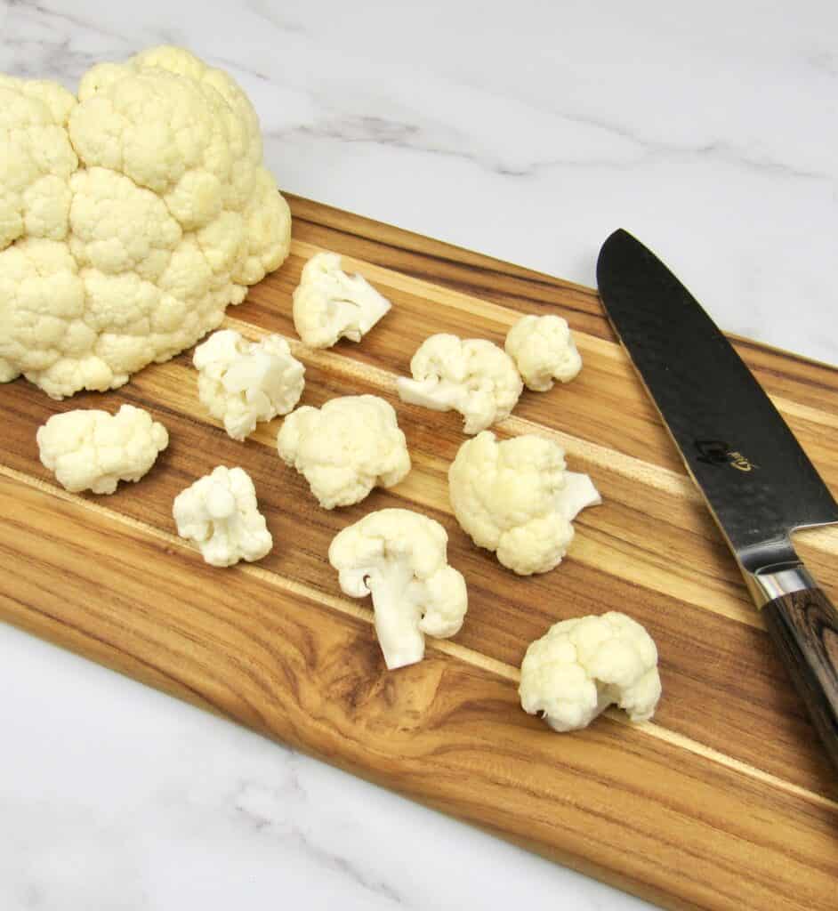 cauliflower florets on cutting board with knife