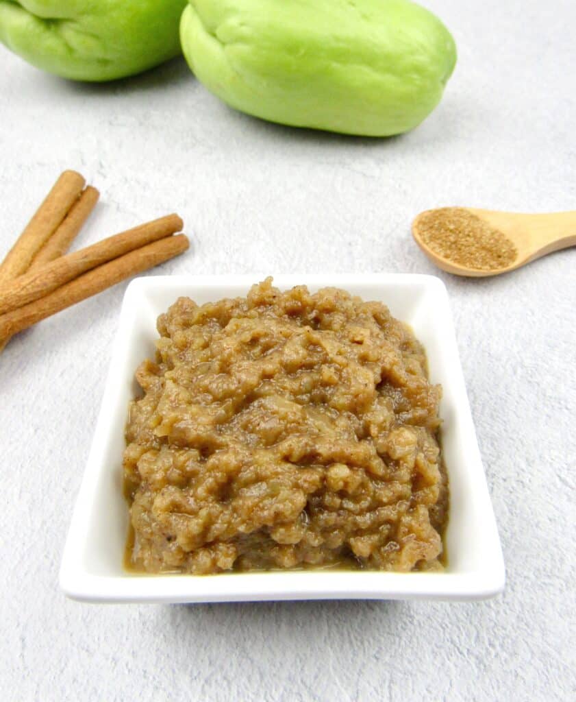 closeup of mock applesauce in white dish with chayote squash and cinnamon in background