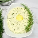 white bowl with mashed cauliflower with rosemary sprig garnish