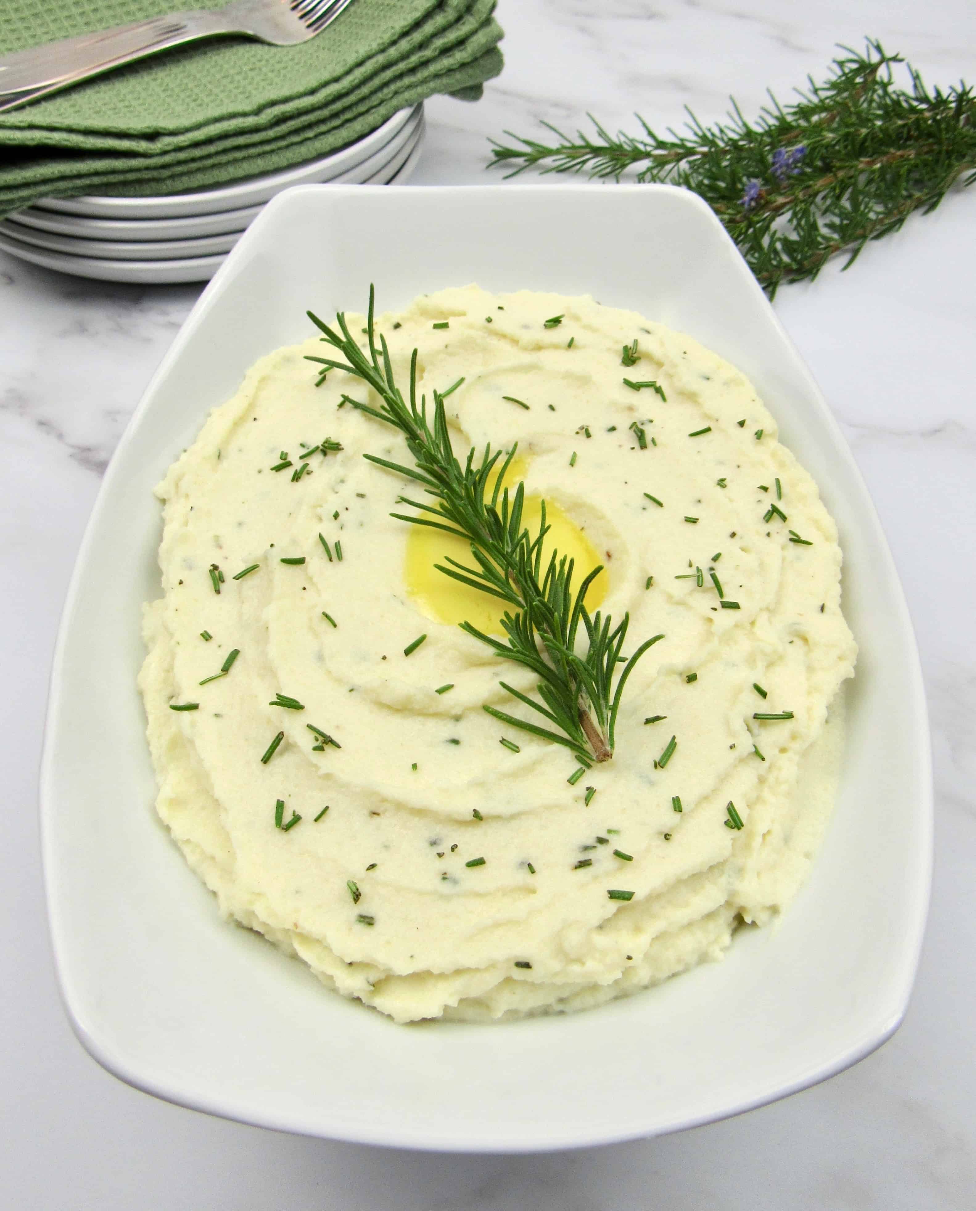 white bowl with mashed cauliflower with rosemary sprig garnish