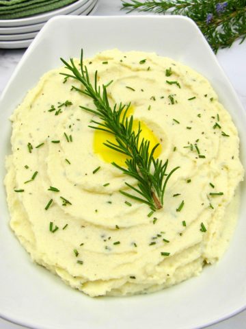 white bowl with mashed cauliflower with rosemary sprig garnish